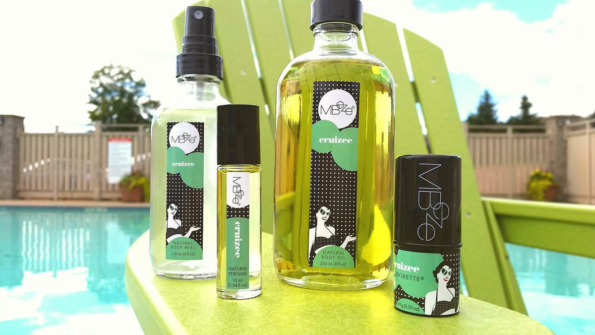 MBeze Cruizee Collection including Body Mist, Perfume, Body Oil, and Deodorette on a big green chair, poolside.