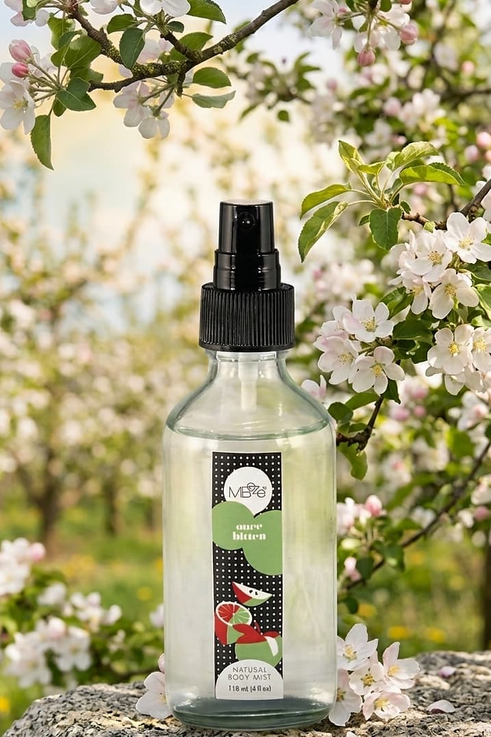 MBeze Once Bitten Body Mist surrounded by apple blossoms.