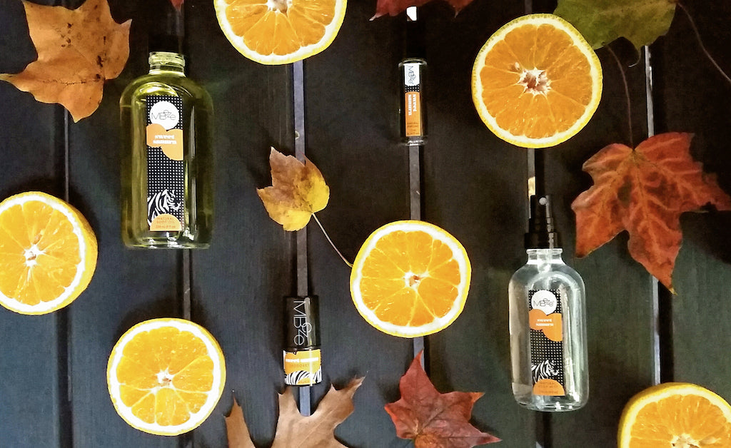 MBeze Sweet Sanura Collections including Body Oil, Deodorette, Perfume, and Body Mist surrounded by autumn leaves and oranges.